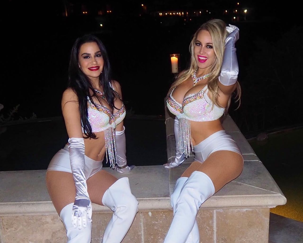 Two models in matching white sequined outfits, posing outdoors at a nightlife event.