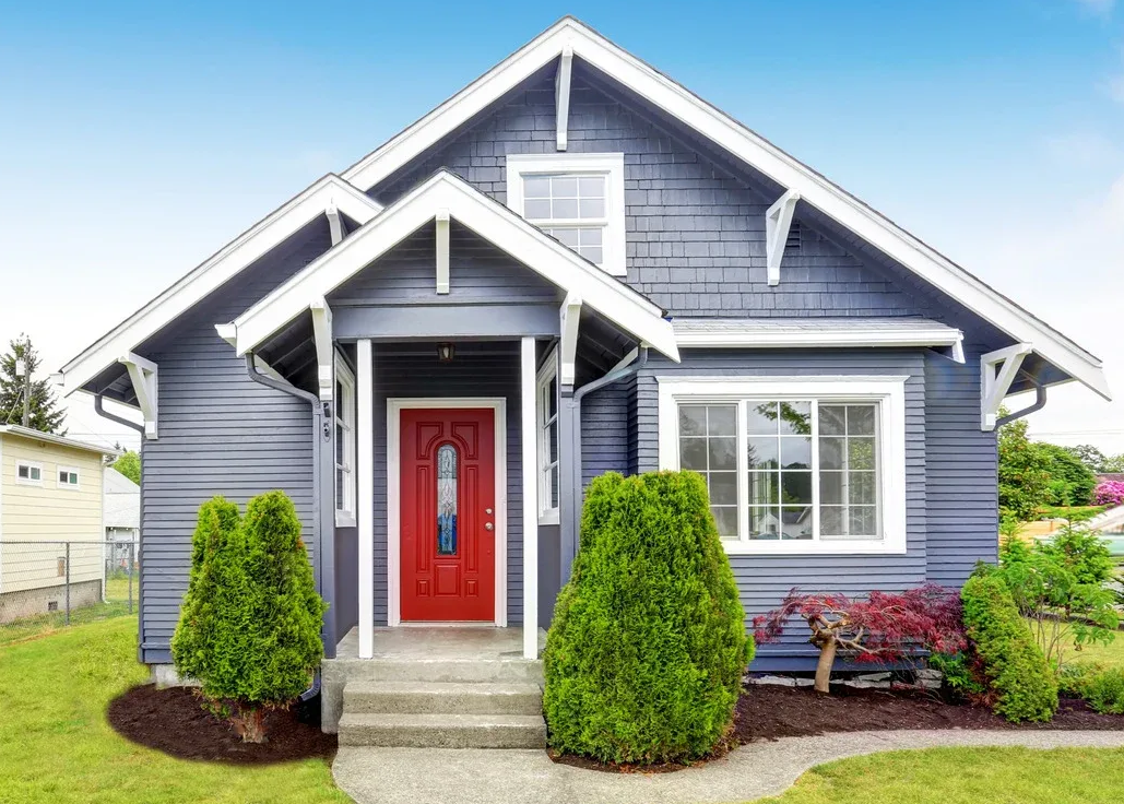 Blue house with white trim, red door, and green bushes.