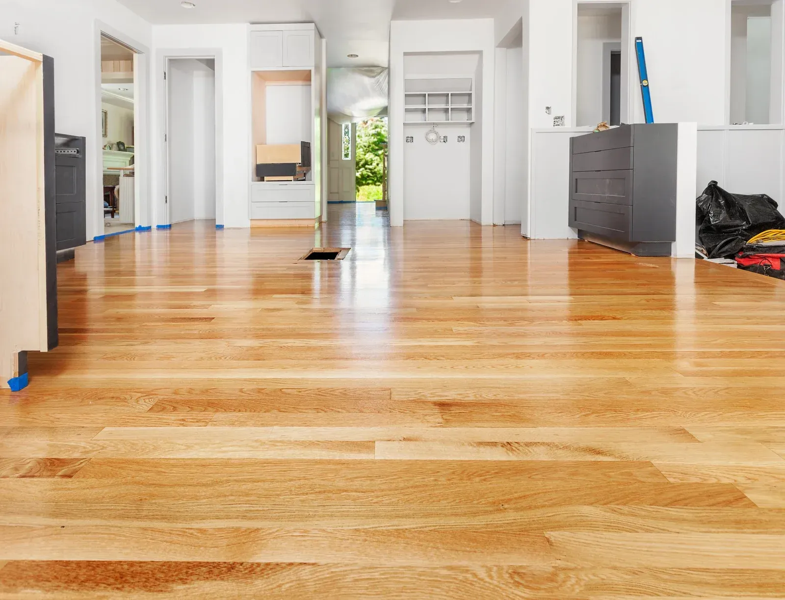 Newly installed hardwood floors in an interior space; light brown planks reflect light. White walls, grey cabinets.