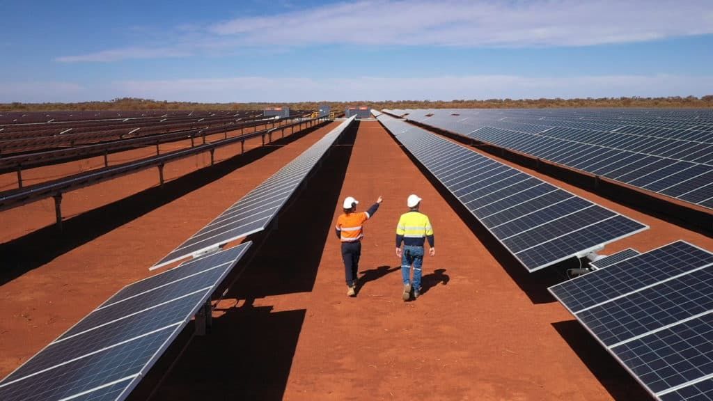 Two men are walking through a field of solar panels.