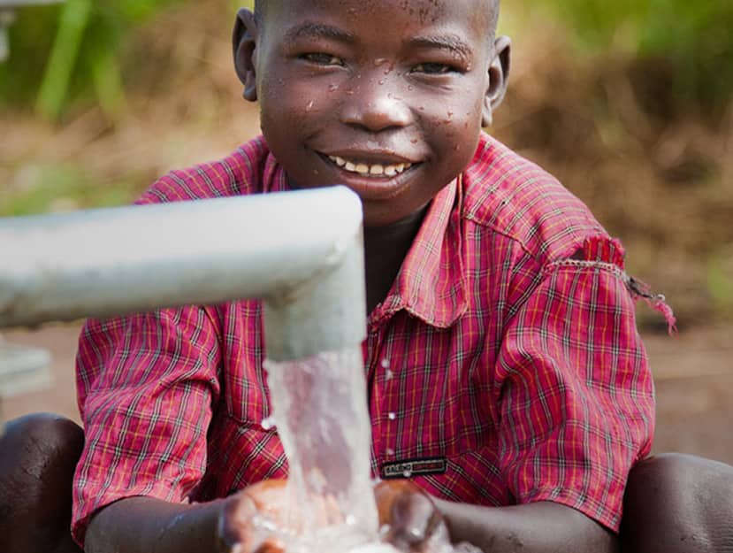 A young boy is washing his hands with water from a pipe.
