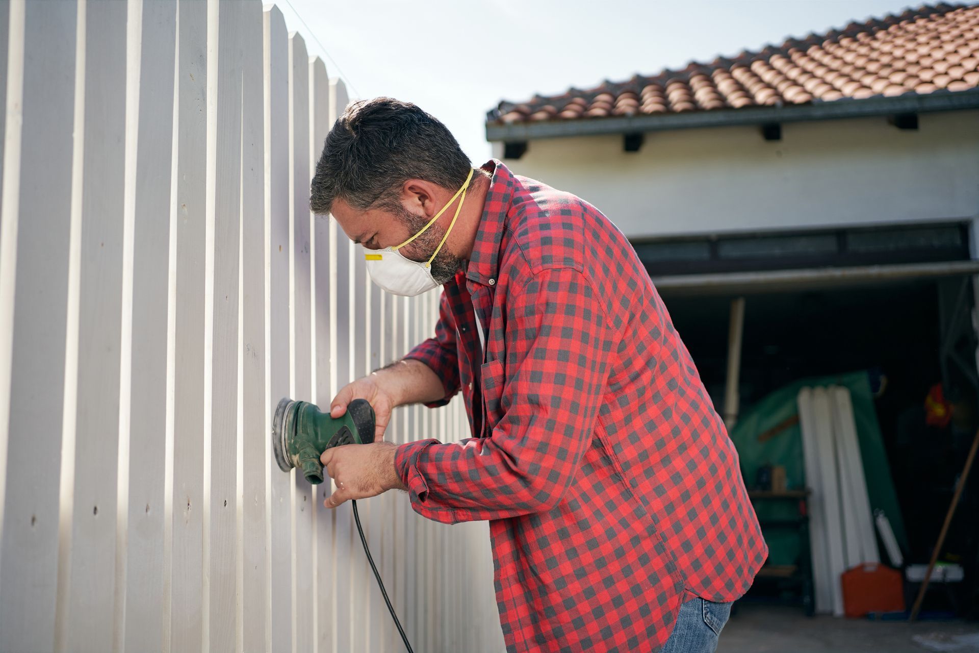 Contractor sanding white wooden fence.