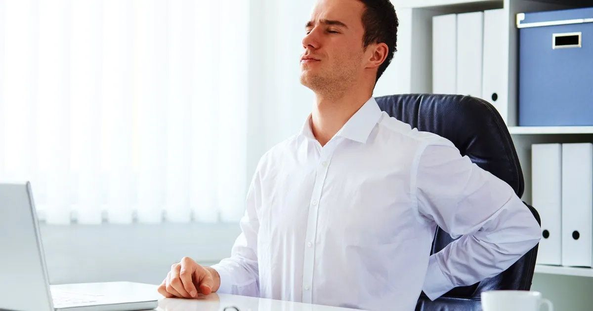 A man is sitting at a desk with his hands on his back.