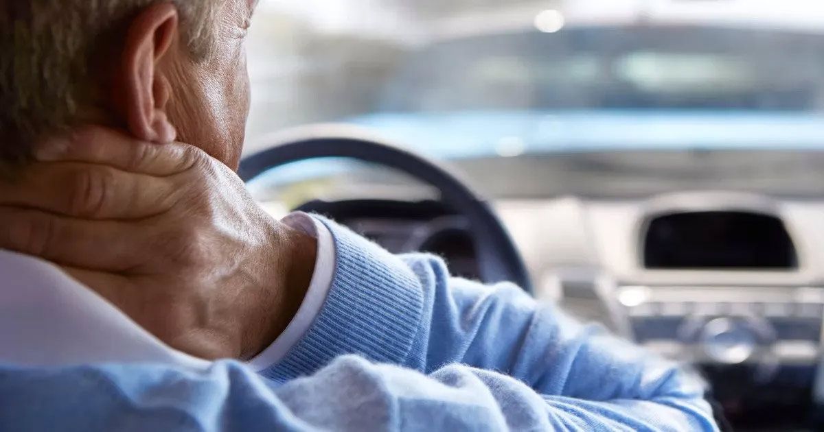 A man is holding his neck while driving a car.