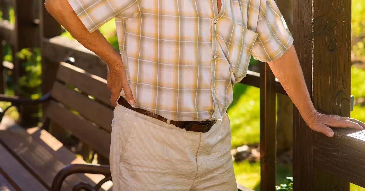 A man in a plaid shirt is standing next to a wooden bench.