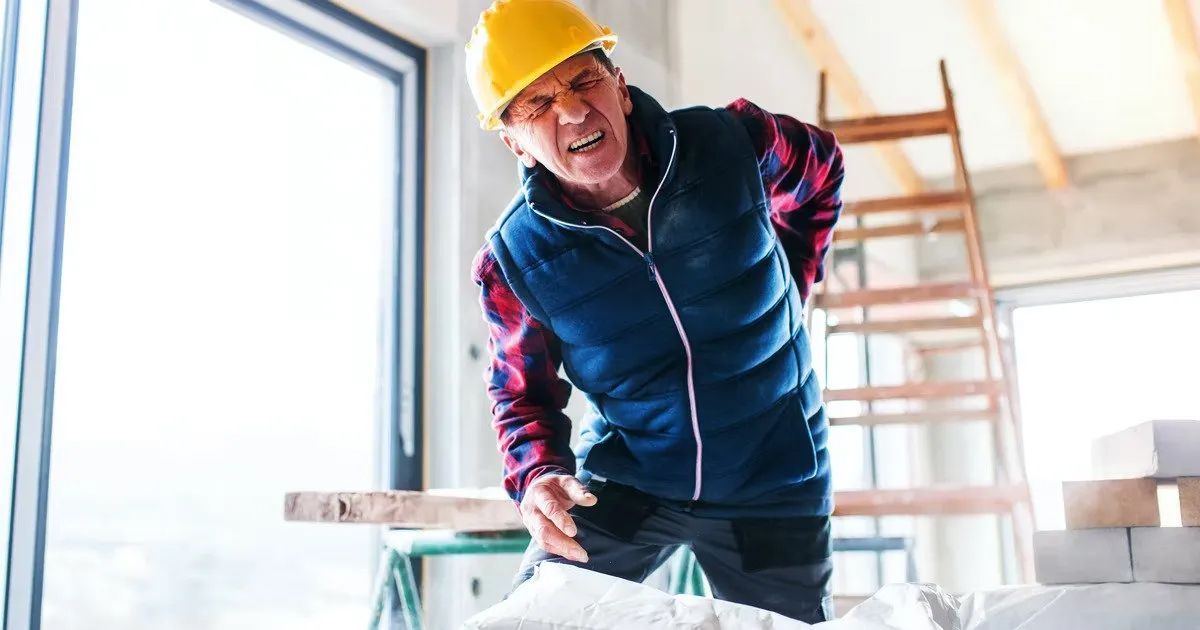 A construction worker is holding his back in pain.