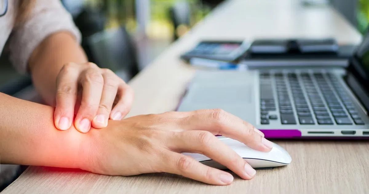 A woman is holding her wrist in pain while using a laptop computer.