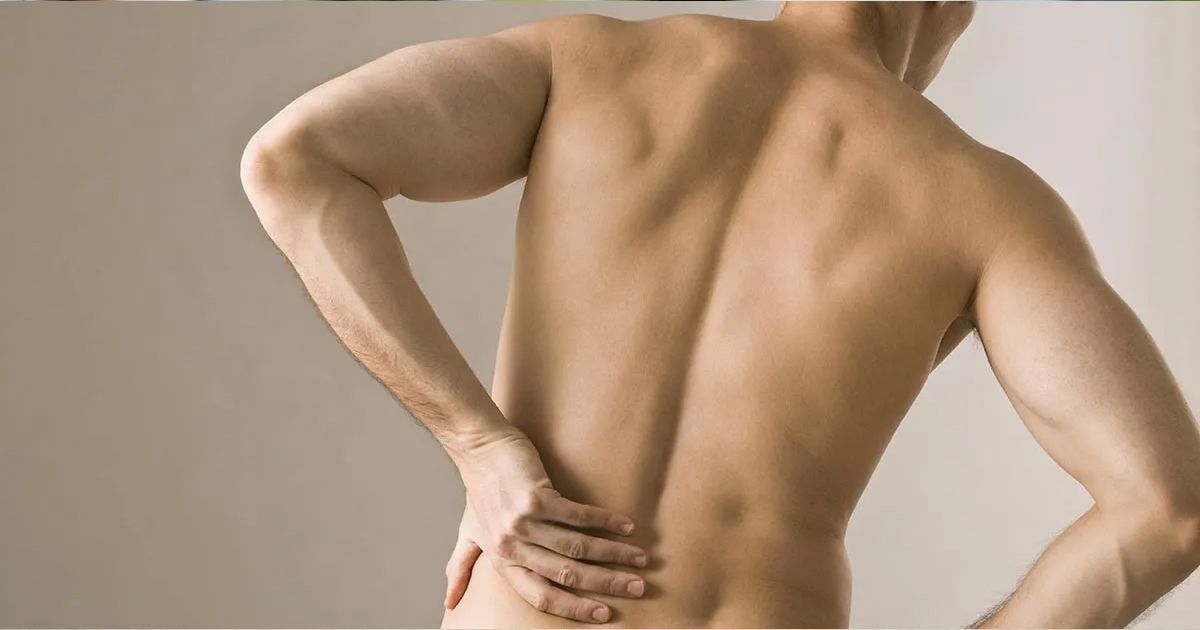 A shirtless man is holding his back in pain.