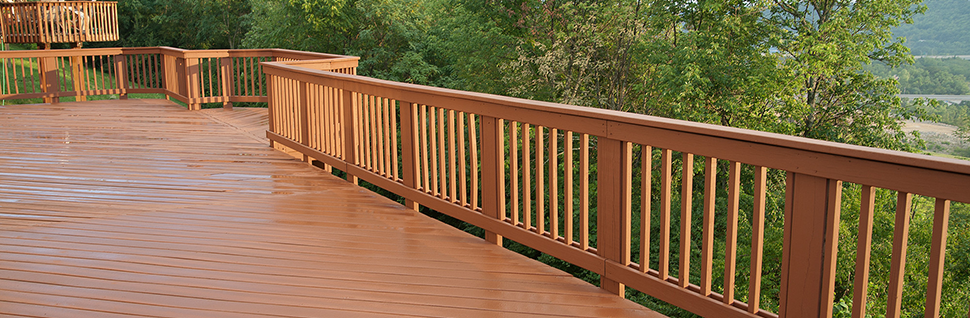 A freshly painted and stained wood deck with railing on a summer afternoon after a rain shower.