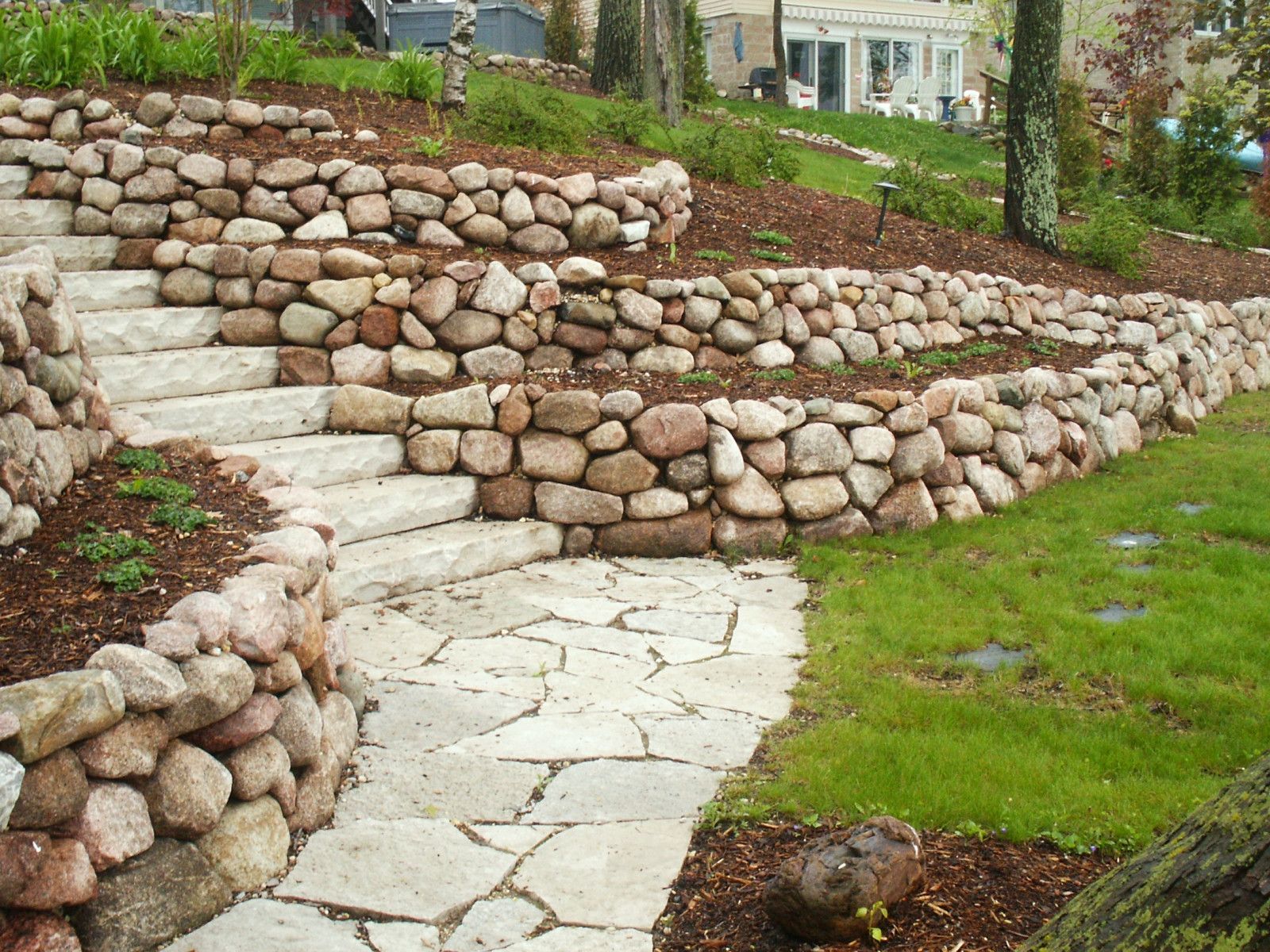 A stone wall and stairs in a garden with a house in the background