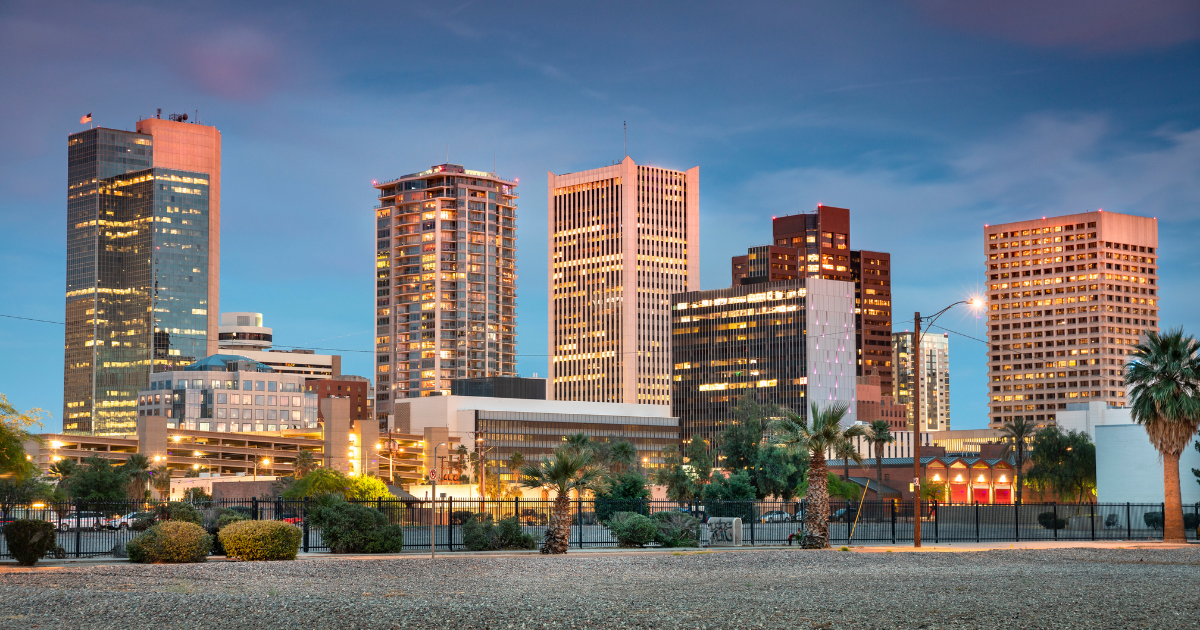 Downtown Phoenix skyline at dusk with lit skyscrapers under a blue sky.