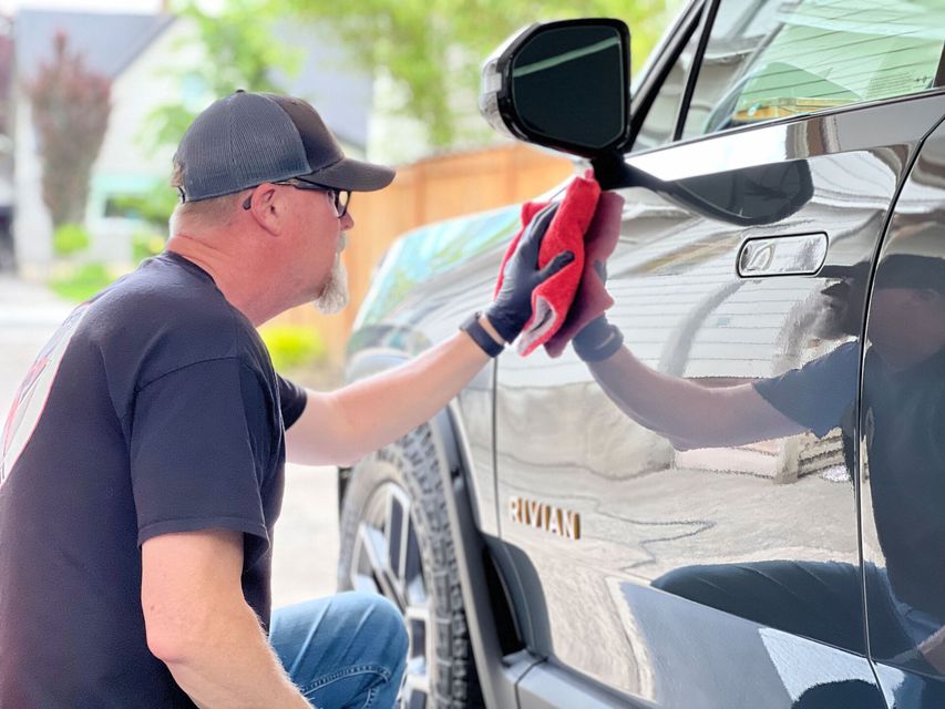 Man wiping a silver SUV with a red cloth in a driveway
