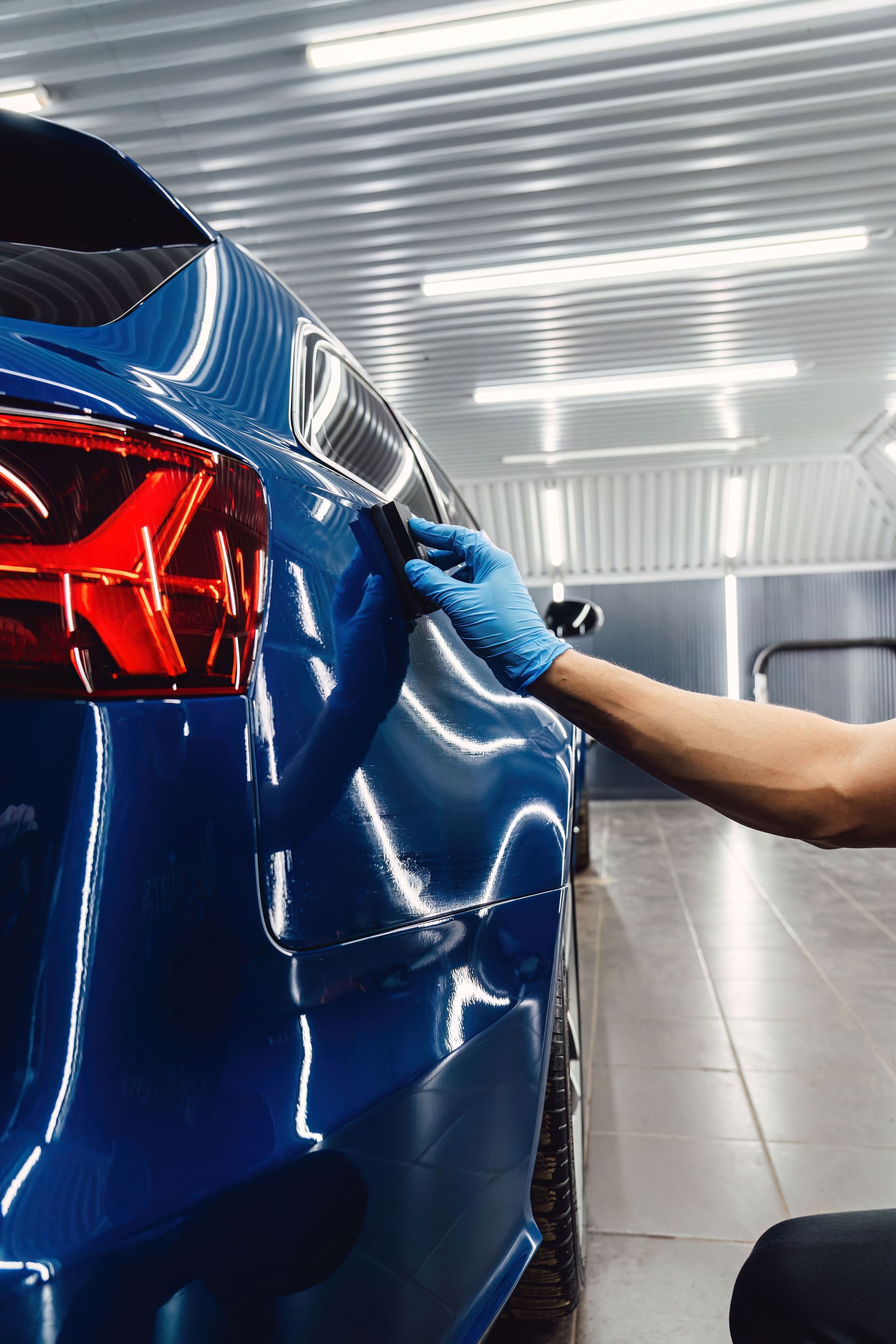 Black-gloved hand polishing a white car hood in a garage