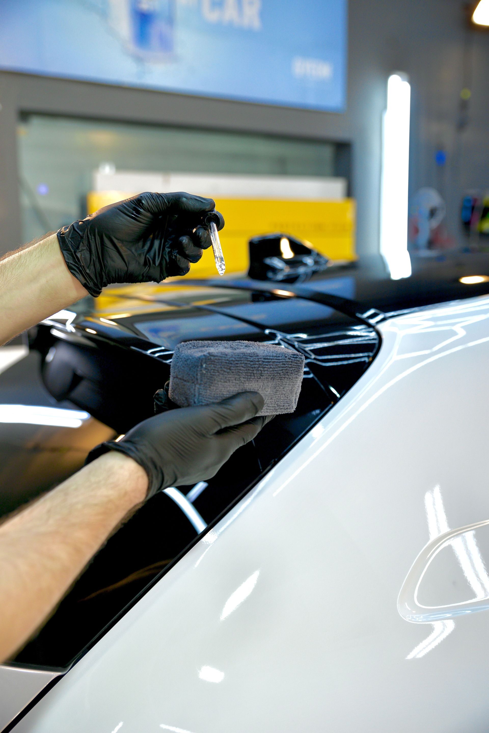 Gloved hands wiping a black car’s glossy surface in a workshop