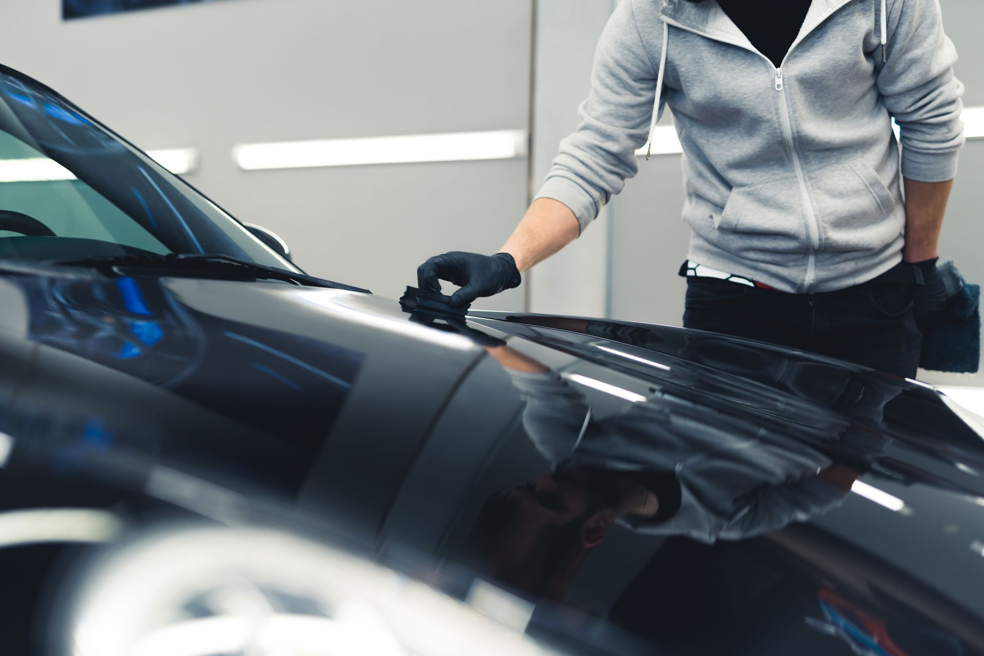 Person in gloves wiping a black car hood with a cloth in a garage