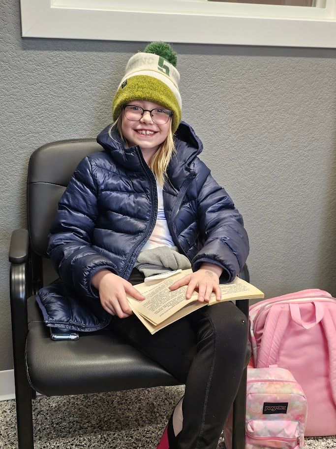 a young girl is sitting in a chair reading a book .