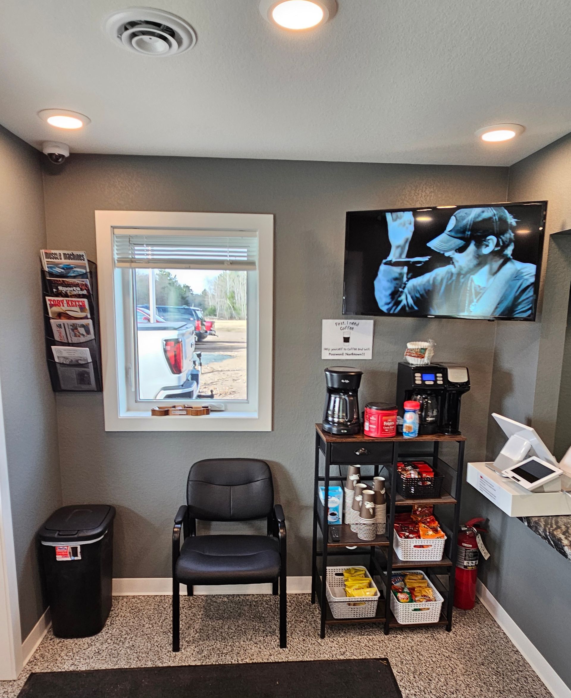 a waiting room with chairs , a trash can , a television and a window .
