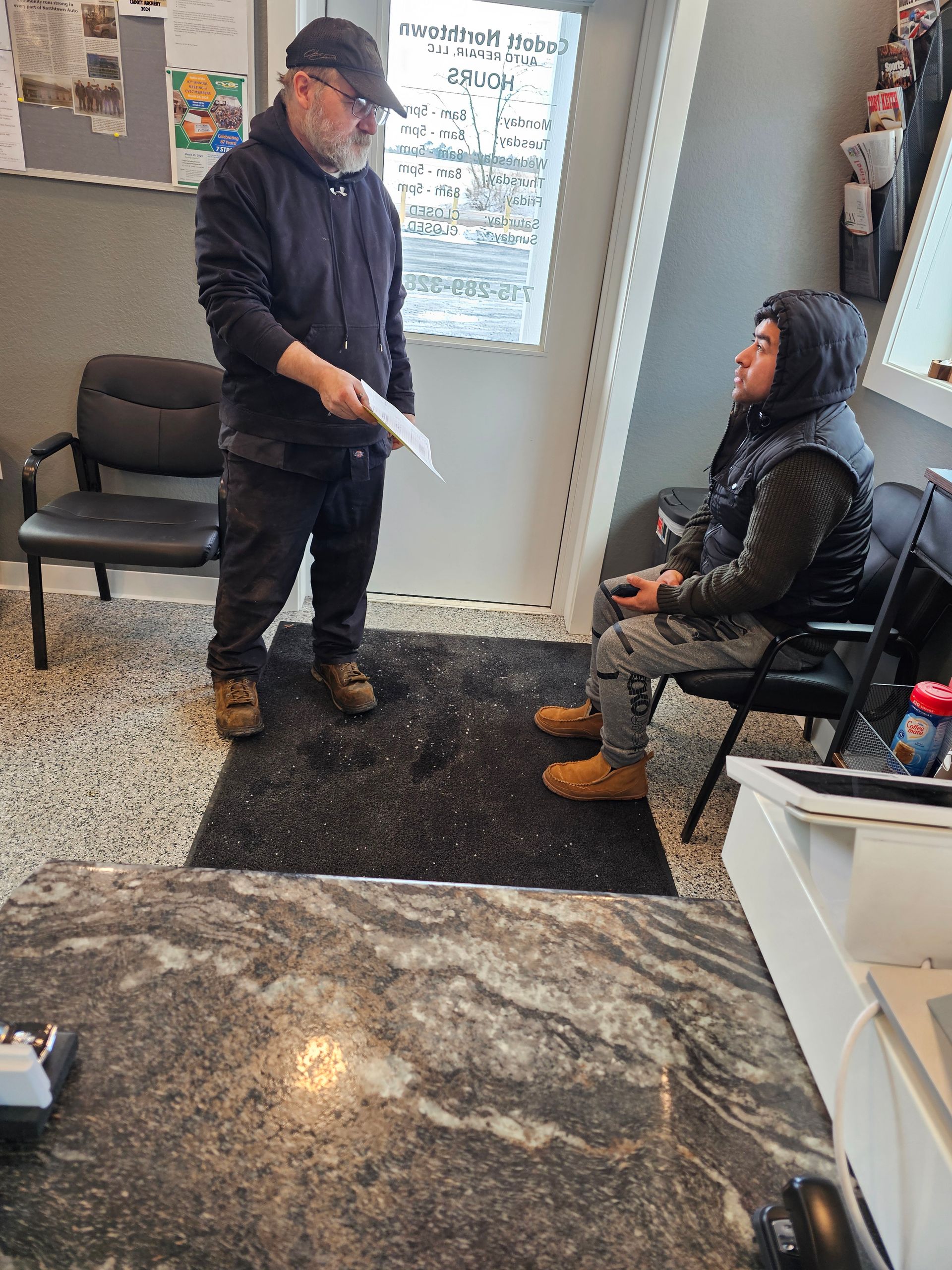 A man is standing next to a woman sitting in a chair in a room.