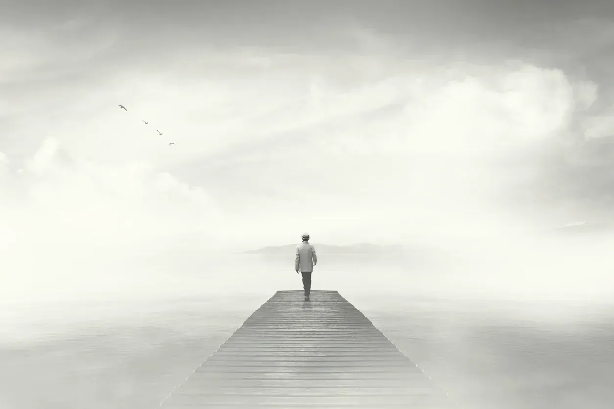 Man walks alone on a wooden pier into a cloudy, ethereal expanse.