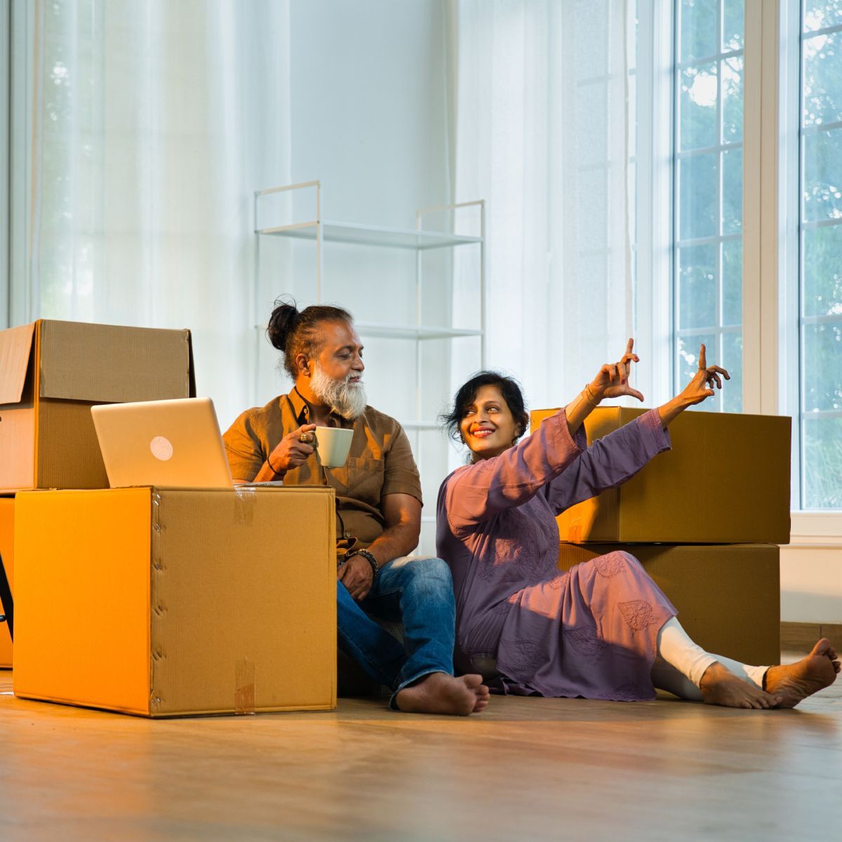 A man and a woman are sitting on the floor surrounded by cardboard boxes.