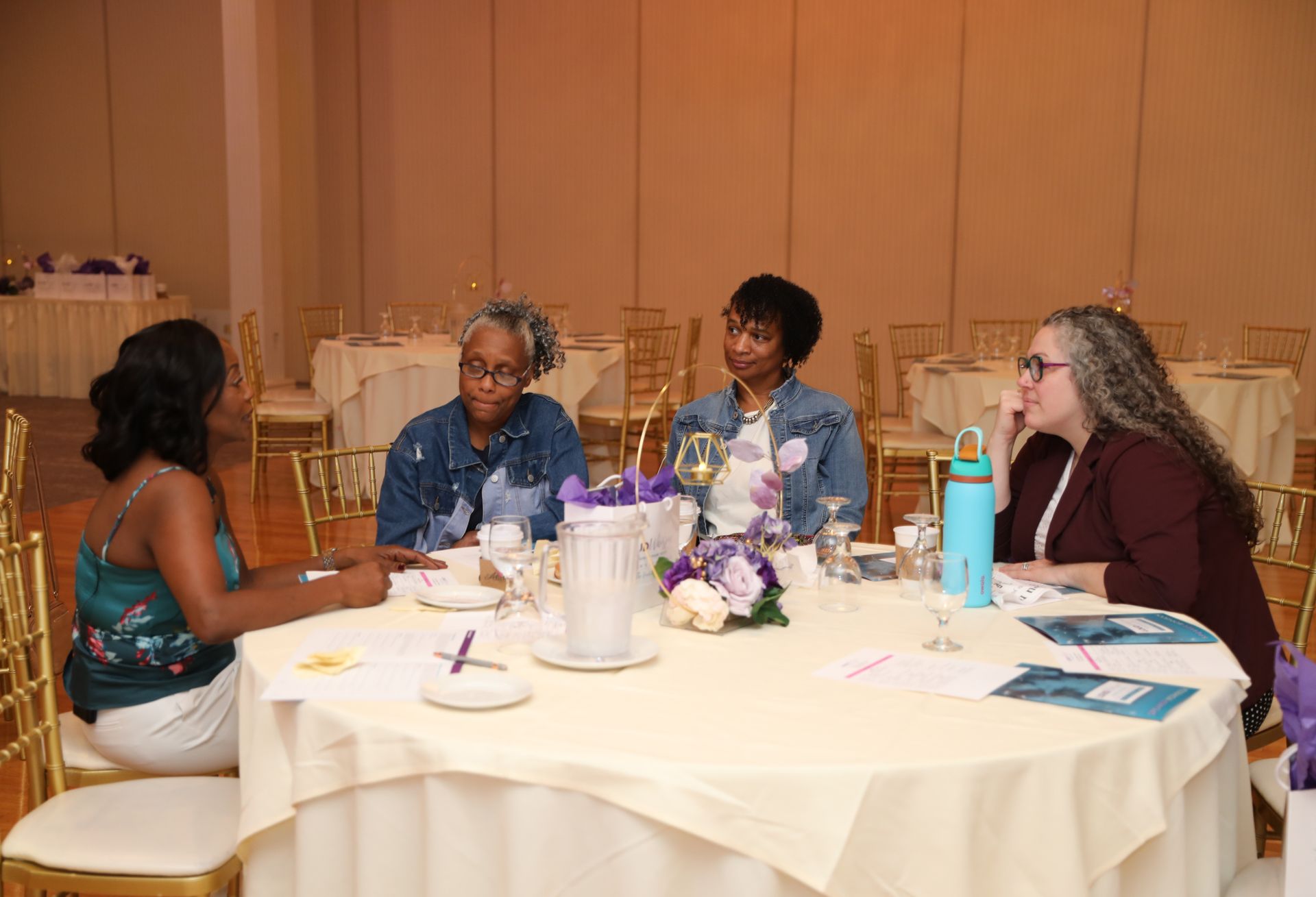 Four people seated around a table in a banquet hall, engaged in conversation.