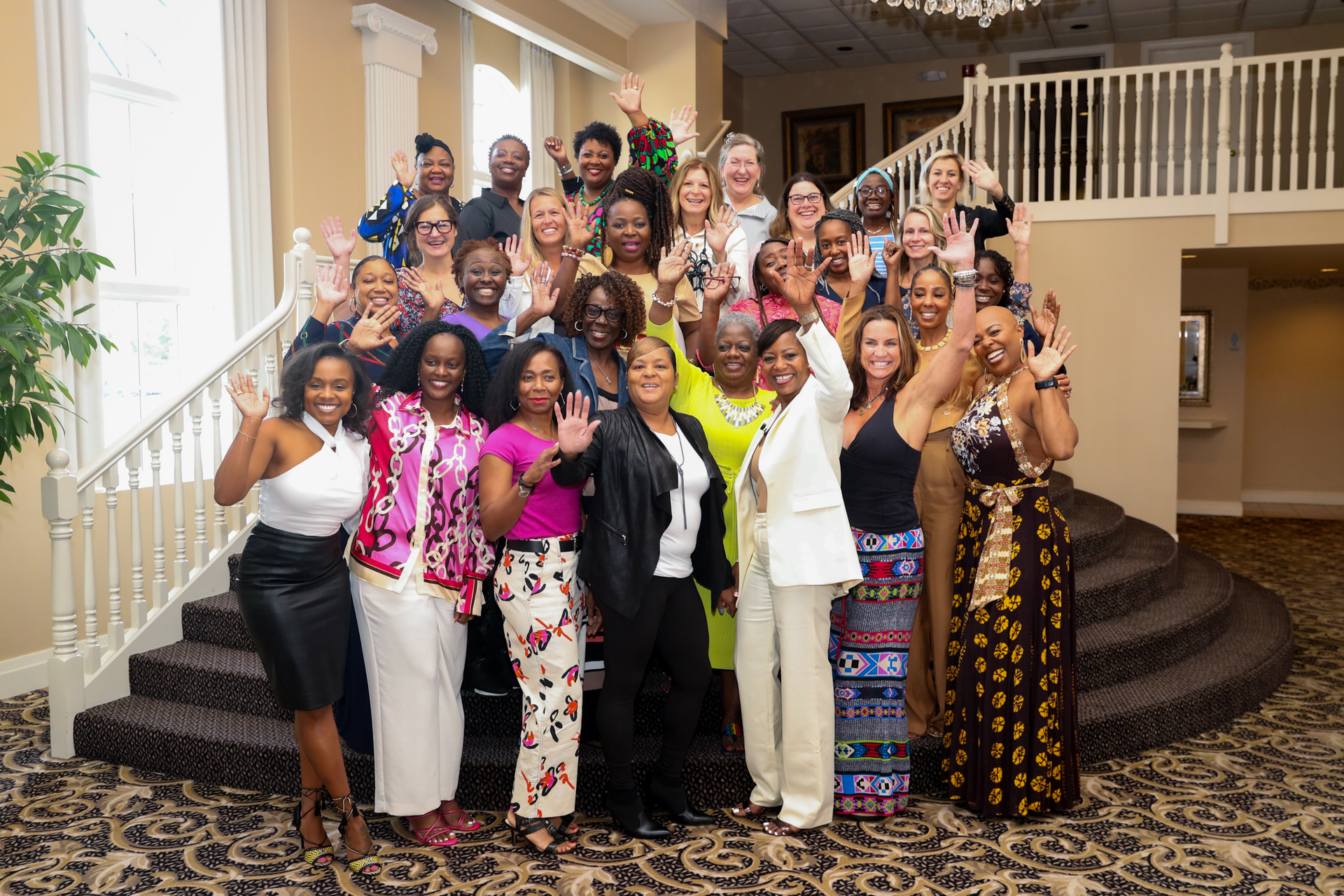 Group of people wave from grand staircase in a well-lit room.