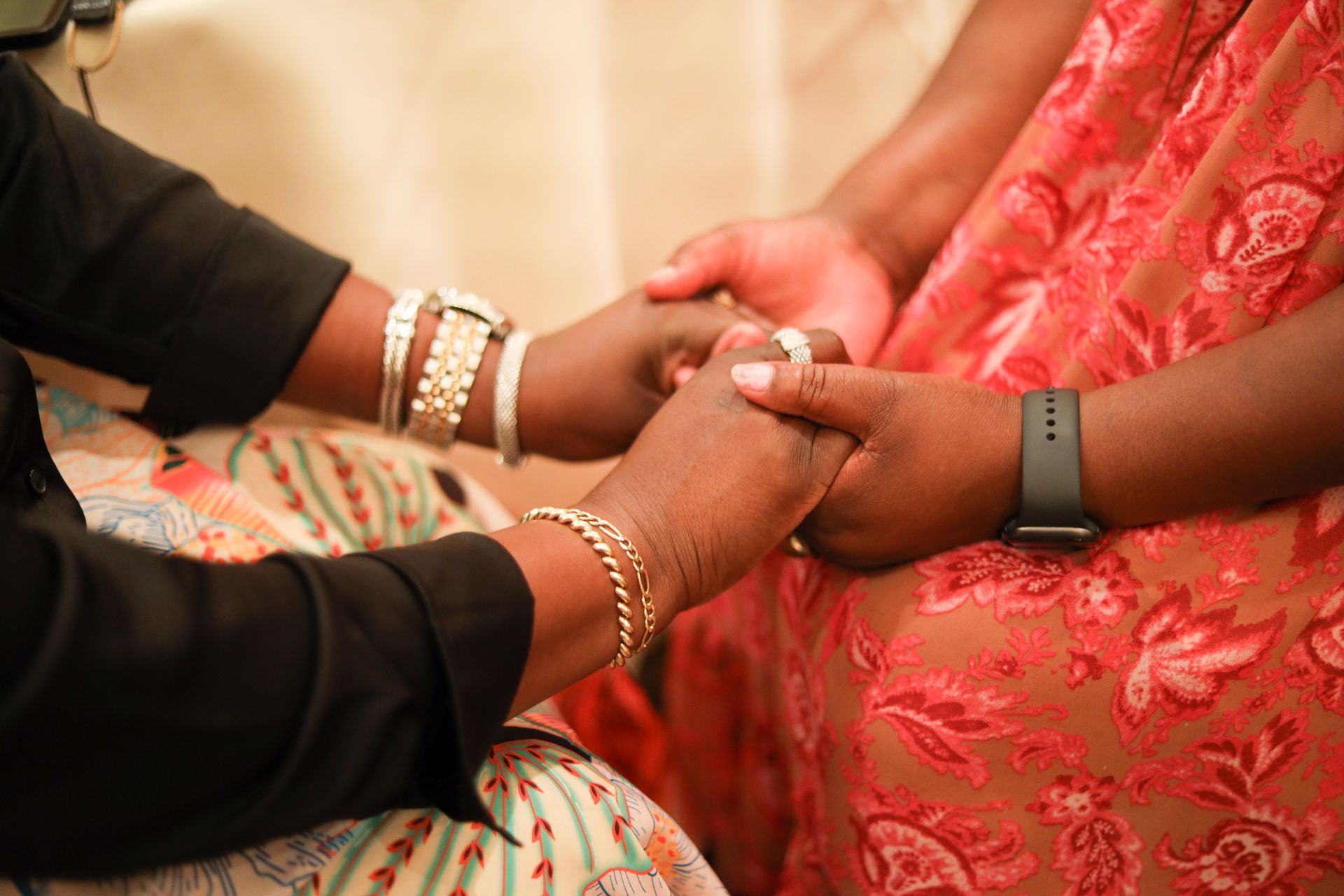 Hands clasped together, one person in black, the other in red floral dress.