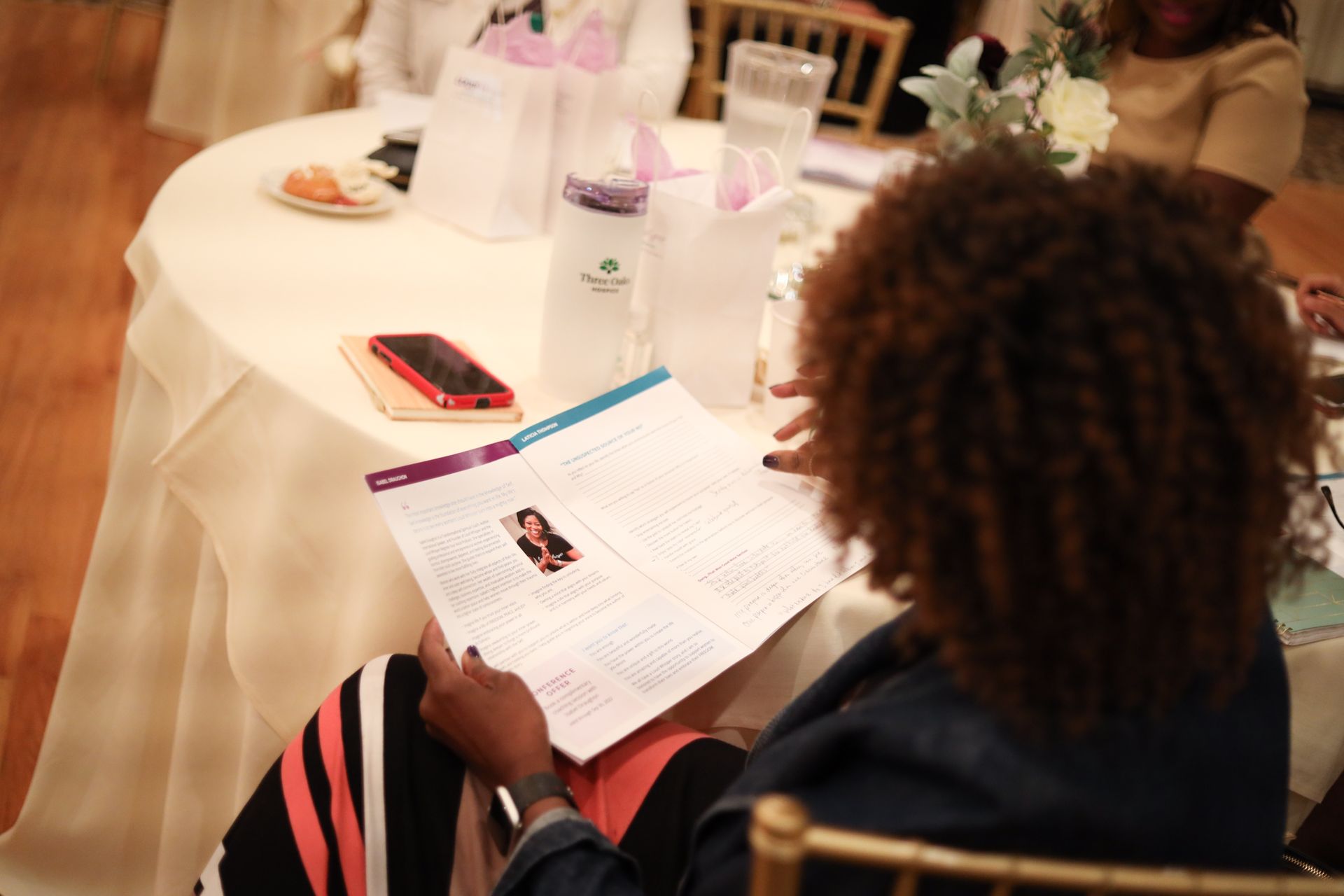 Person reading a document at a table, with bags and phone nearby.