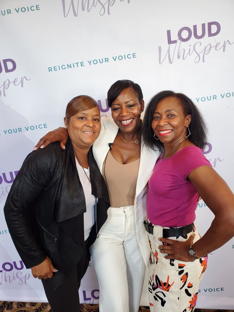 Three women smiling, posing in front of a backdrop with 