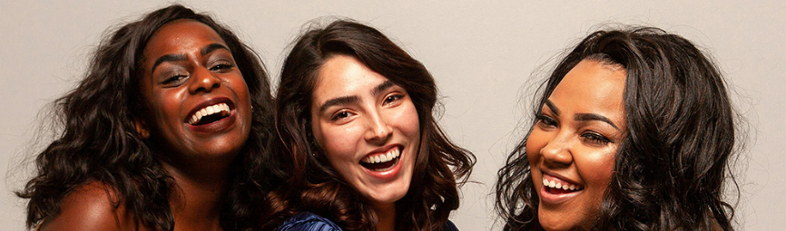 Three smiling women with dark hair against a light background.