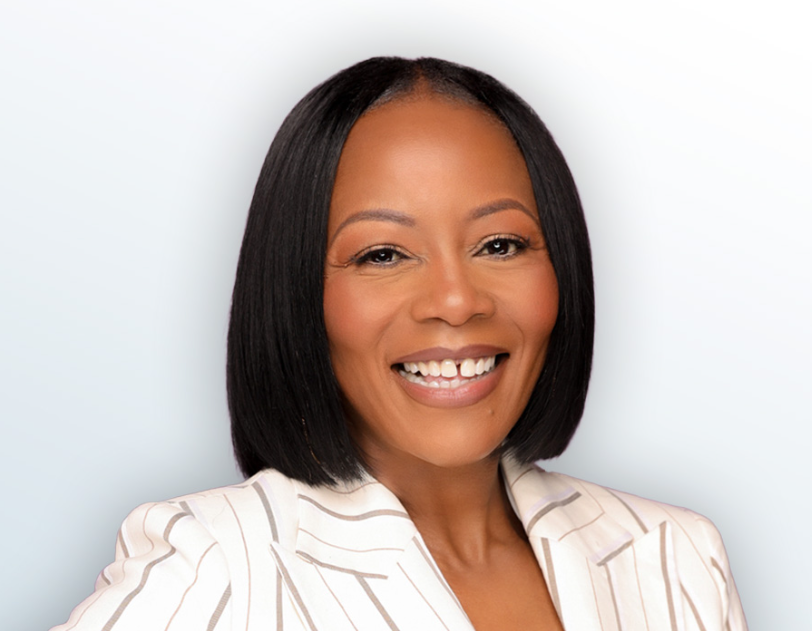 Woman with dark hair, smiling, wearing a striped blazer, on a light blue background.