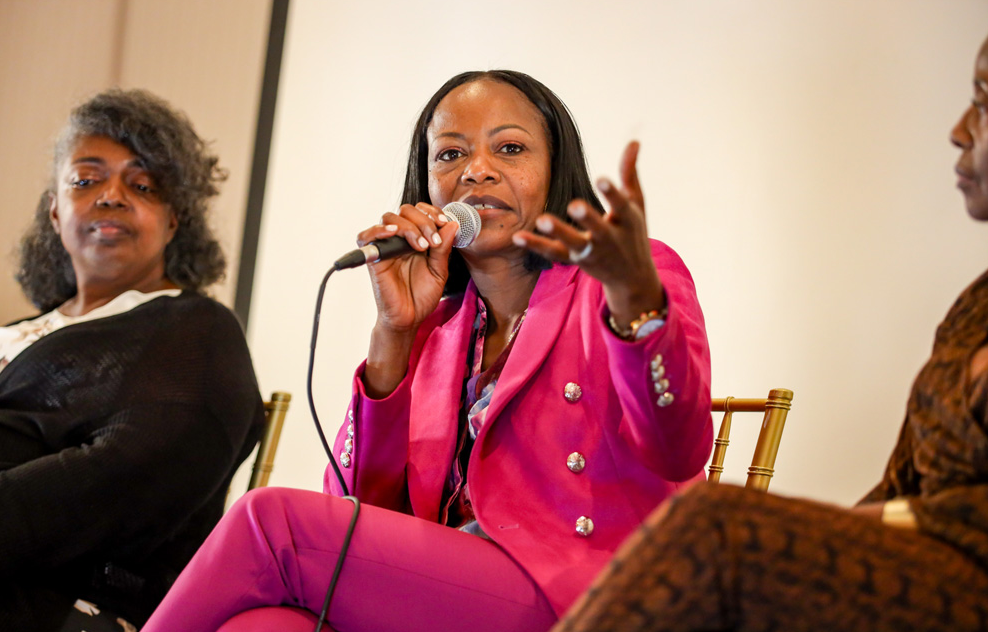 Woman in pink blazer speaks into a microphone at a panel discussion.