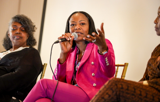 Woman in pink blazer speaks into a microphone at a panel discussion.