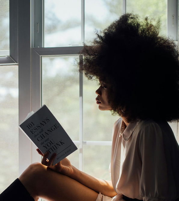 Person with large afro reads book by a window, titled 