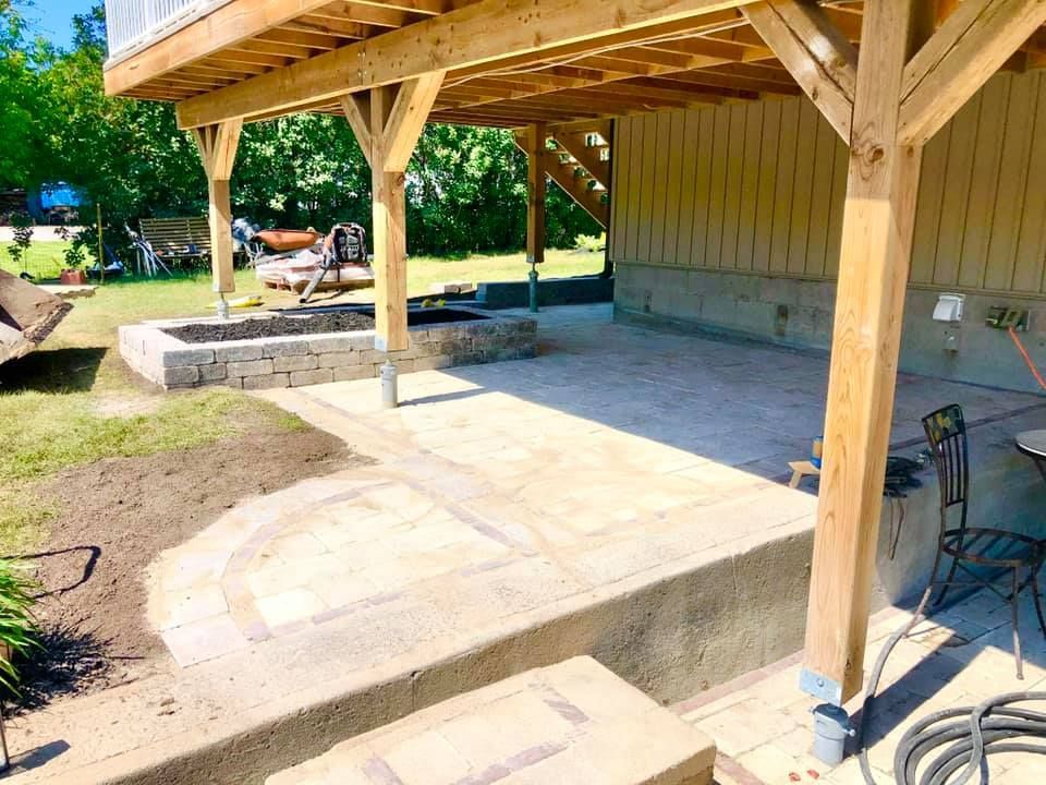 A patio under a wooden deck with a fire pit in the backyard.
