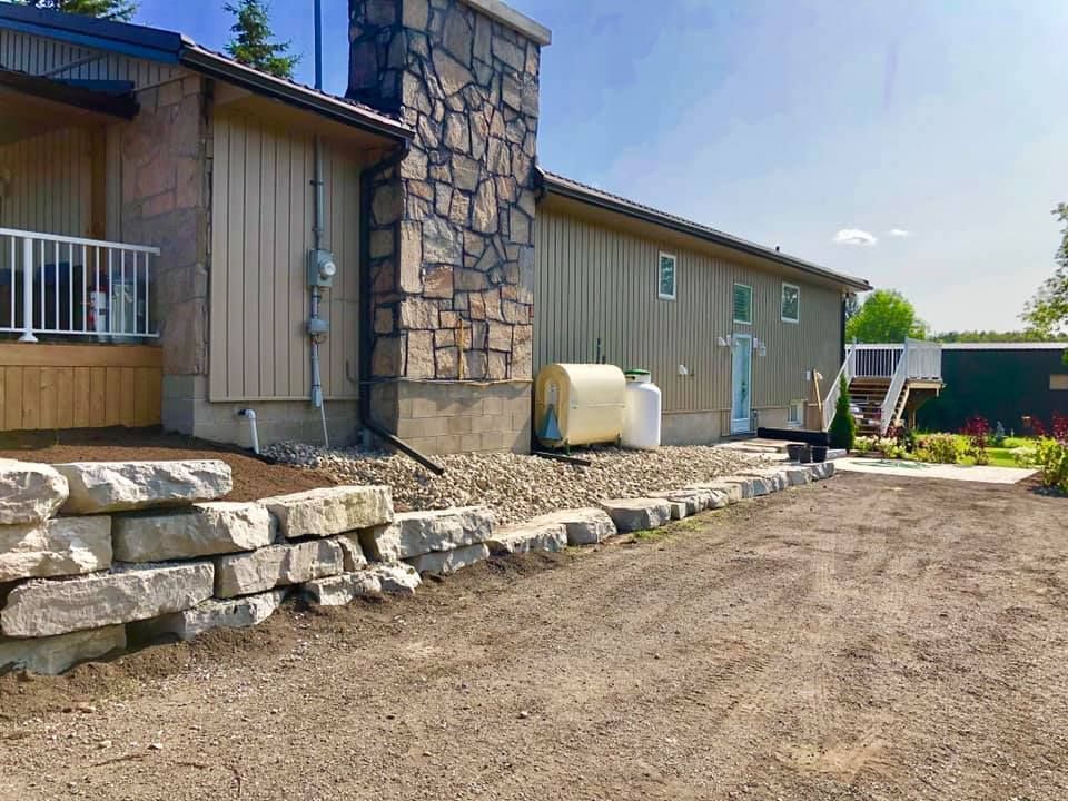 A house with a stone wall and a propane tank in front of it.