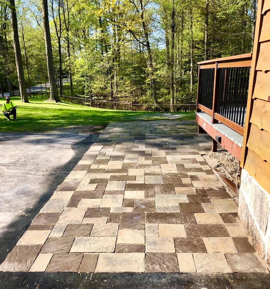 A brick walkway leading to a wooden deck in the woods.