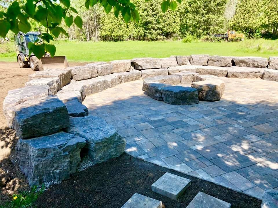 A circular stone patio with a fire pit and a bulldozer in the background.
