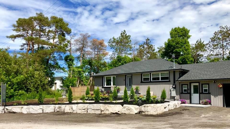A large house with a gray roof is surrounded by trees on a sunny day.
