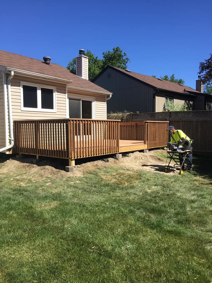 A man is working on a wooden deck in the backyard of a house.