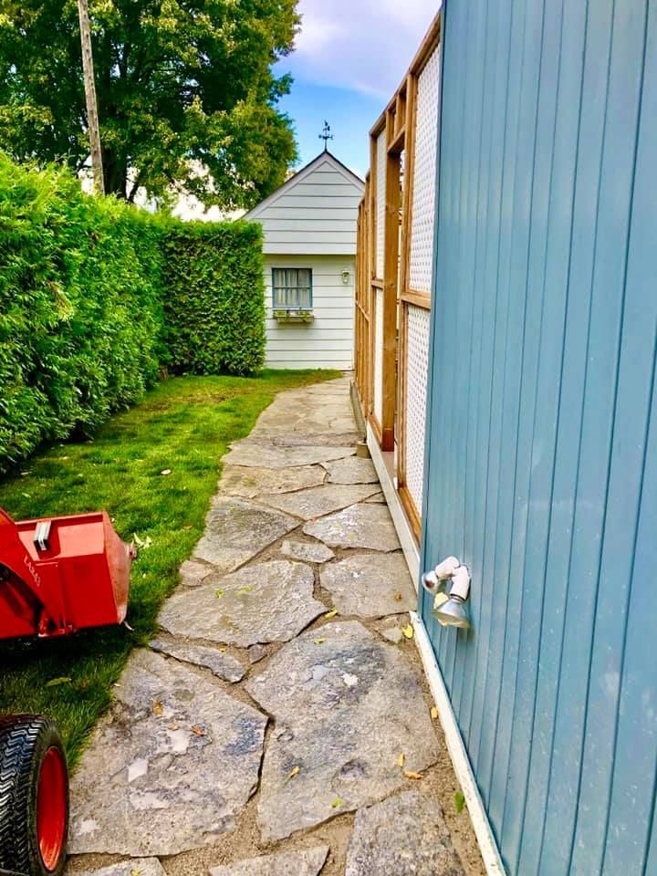 A red snow blower is parked on the side of a stone walkway next to a blue building.