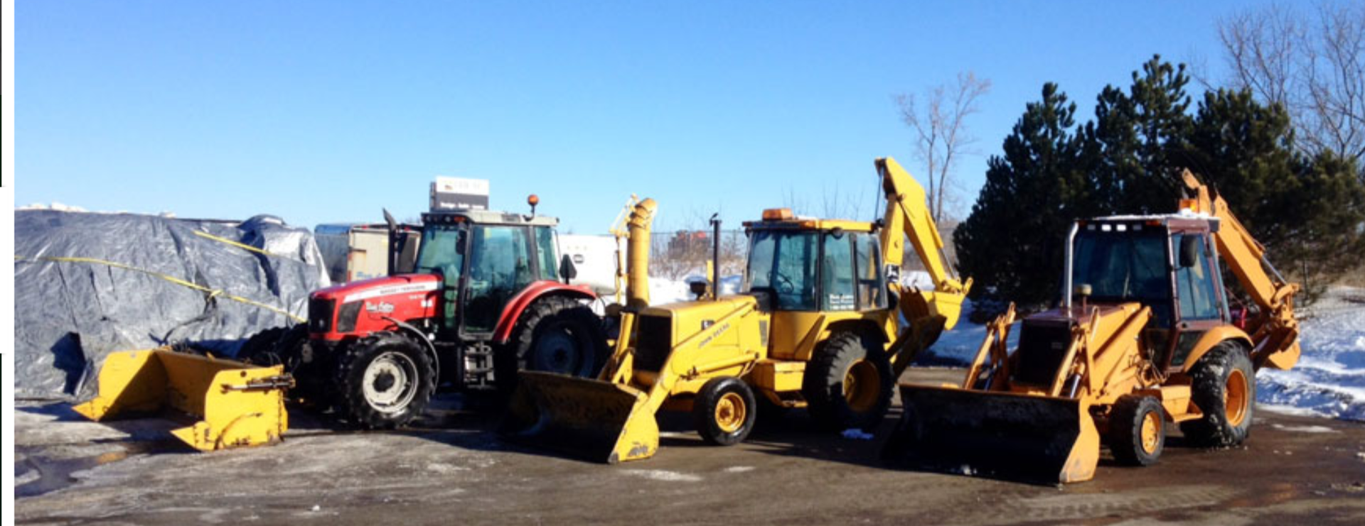 A row of yellow and red tractors are parked in the snow