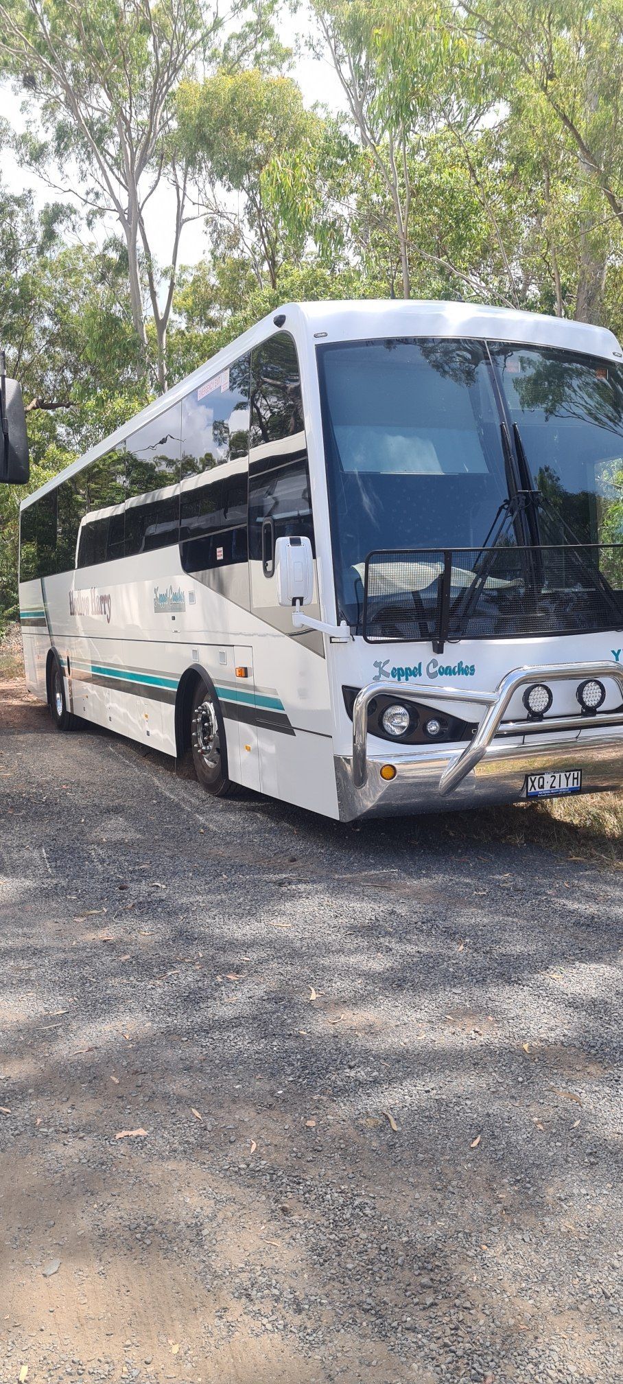 A white coach bus parked on gravel, with trees in the background — Keppel Coaches in Barmaryee, QLD