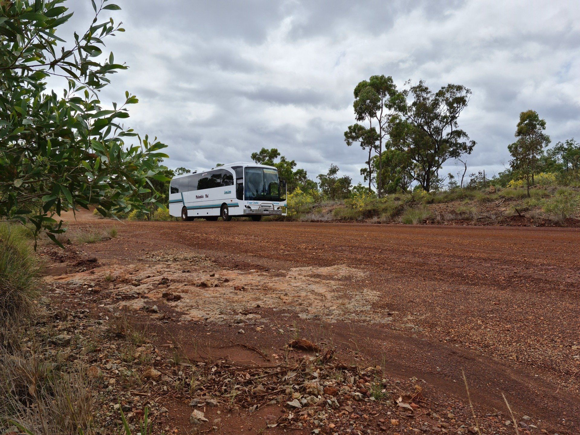 Bus on a Red Dirt Road in a Natural Setting Under a Cloudy Sky — Keppel Coaches in Barmaryee, QLD
