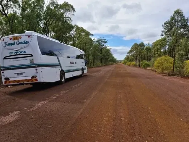 White Bus Parked on A Red Dirt Road Surrounded by Trees Under a Cloudy Sky — Keppel Coaches in Barmaryee, QLD