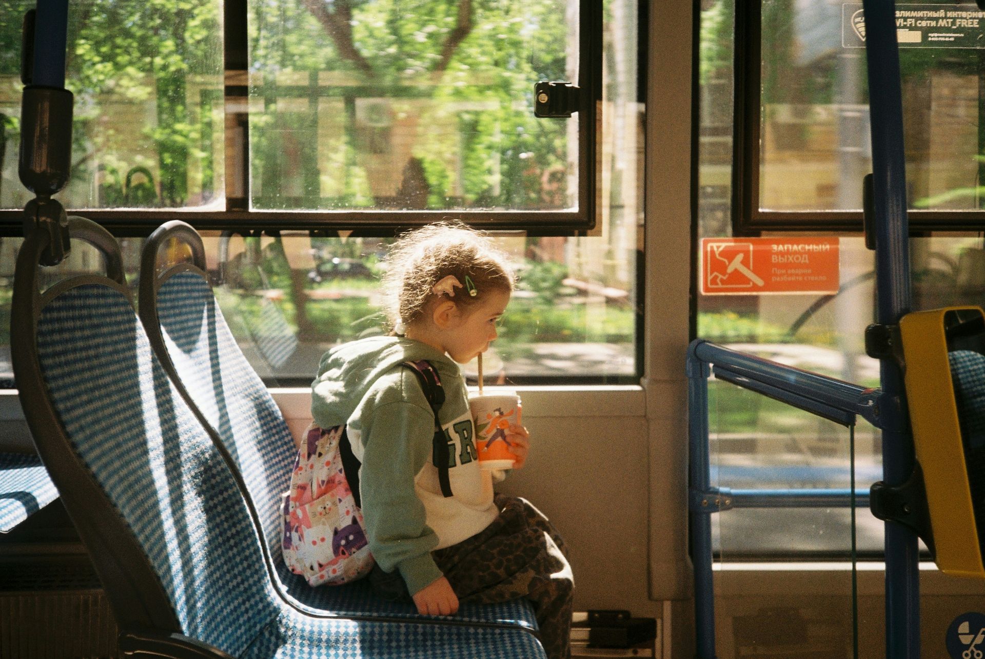 Child on a bus, holding a drink, looking out the window. Sunlight streams through the glass — Keppel Coaches in Barmaryee, QLD