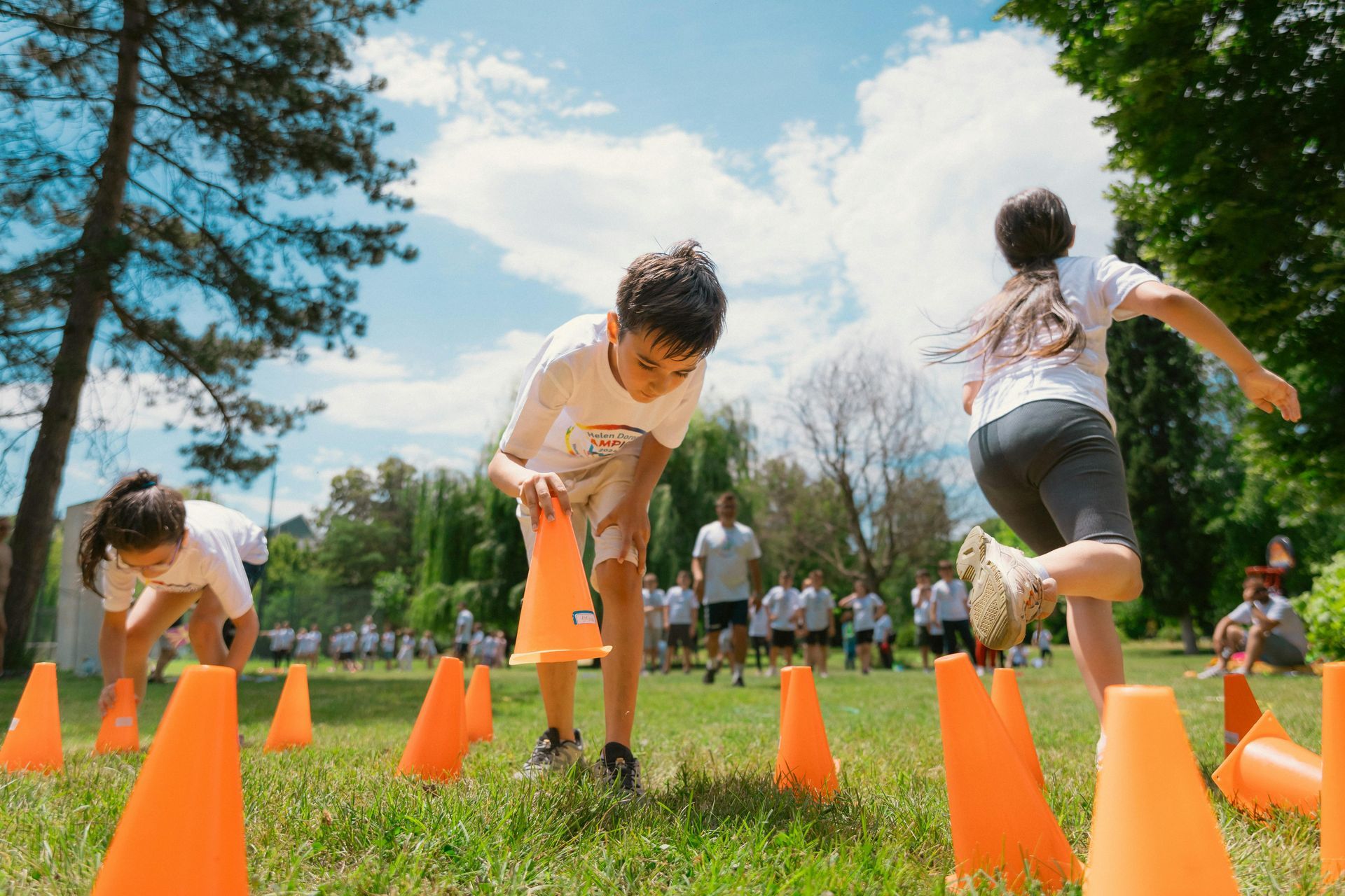Children playing an outdoor game with orange cones. One boy picks up a cone while two others run. Green grass, blue sky — Keppel Coaches in Barmaryee, QLD