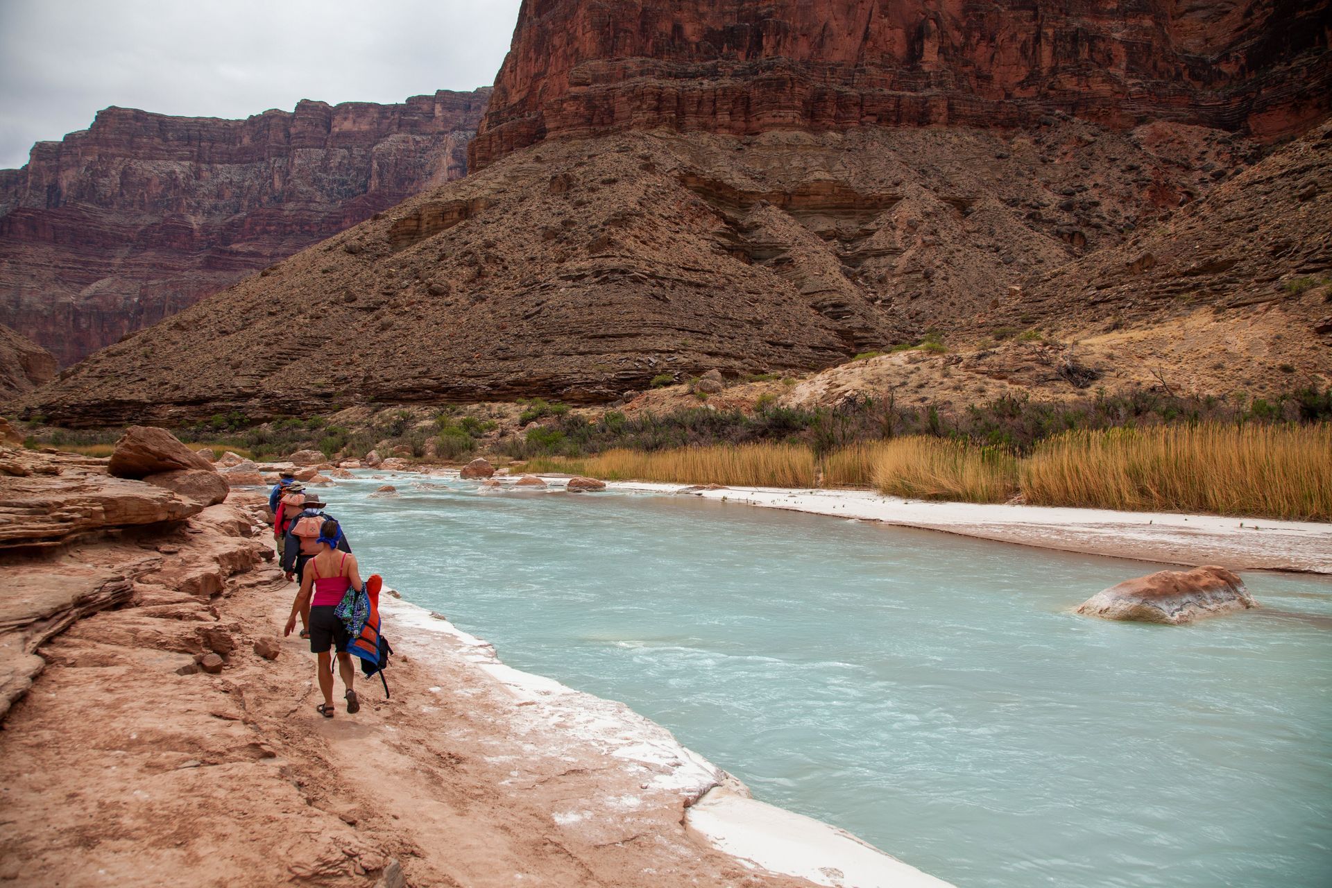 Hikers walking along a river in a canyon. Brown rocks and turquoise water.