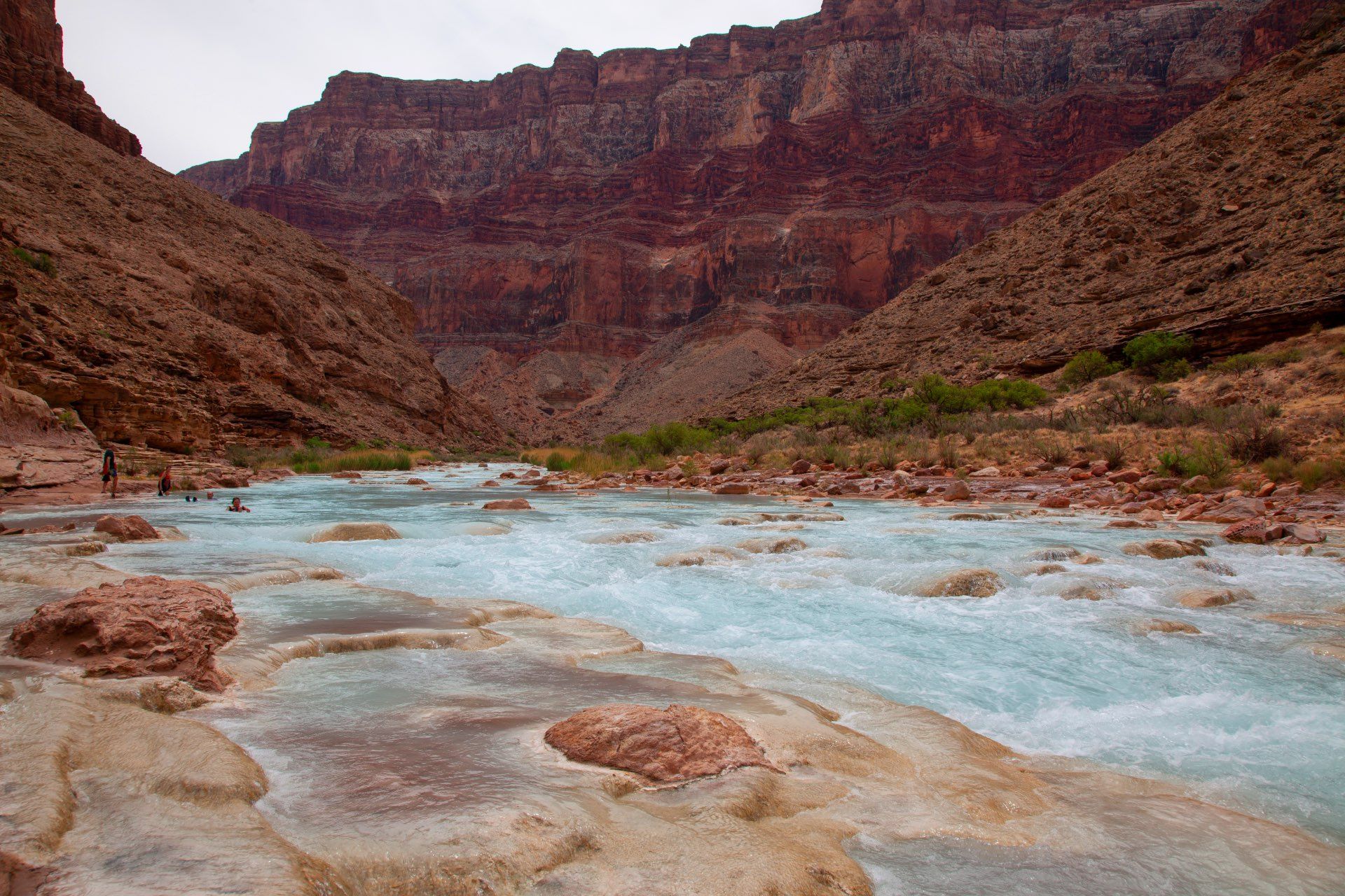 A turquoise river flows through a canyon with red rock walls.