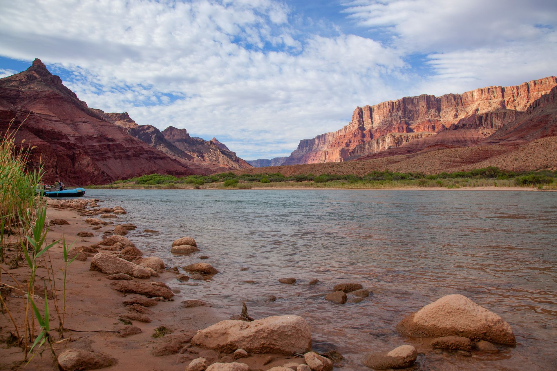 River flowing between red rock canyon walls under a cloudy blue sky.